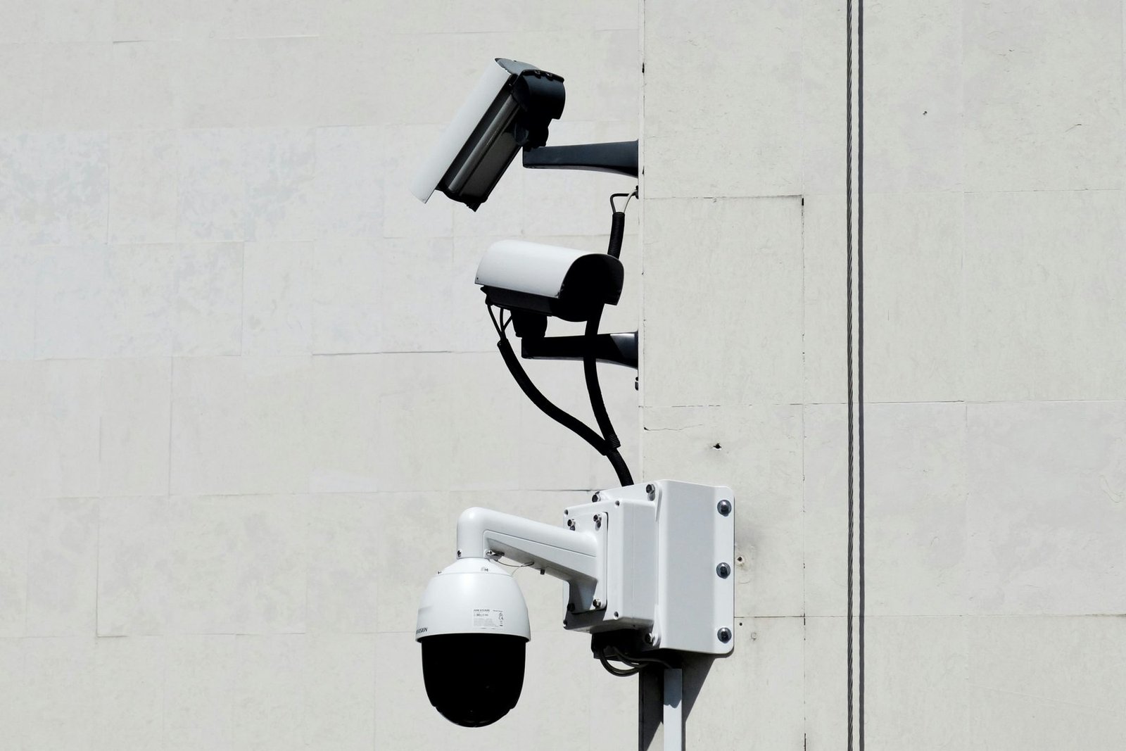 Three cameras mounted high on a plain wall, well above head height, angled steeply downward