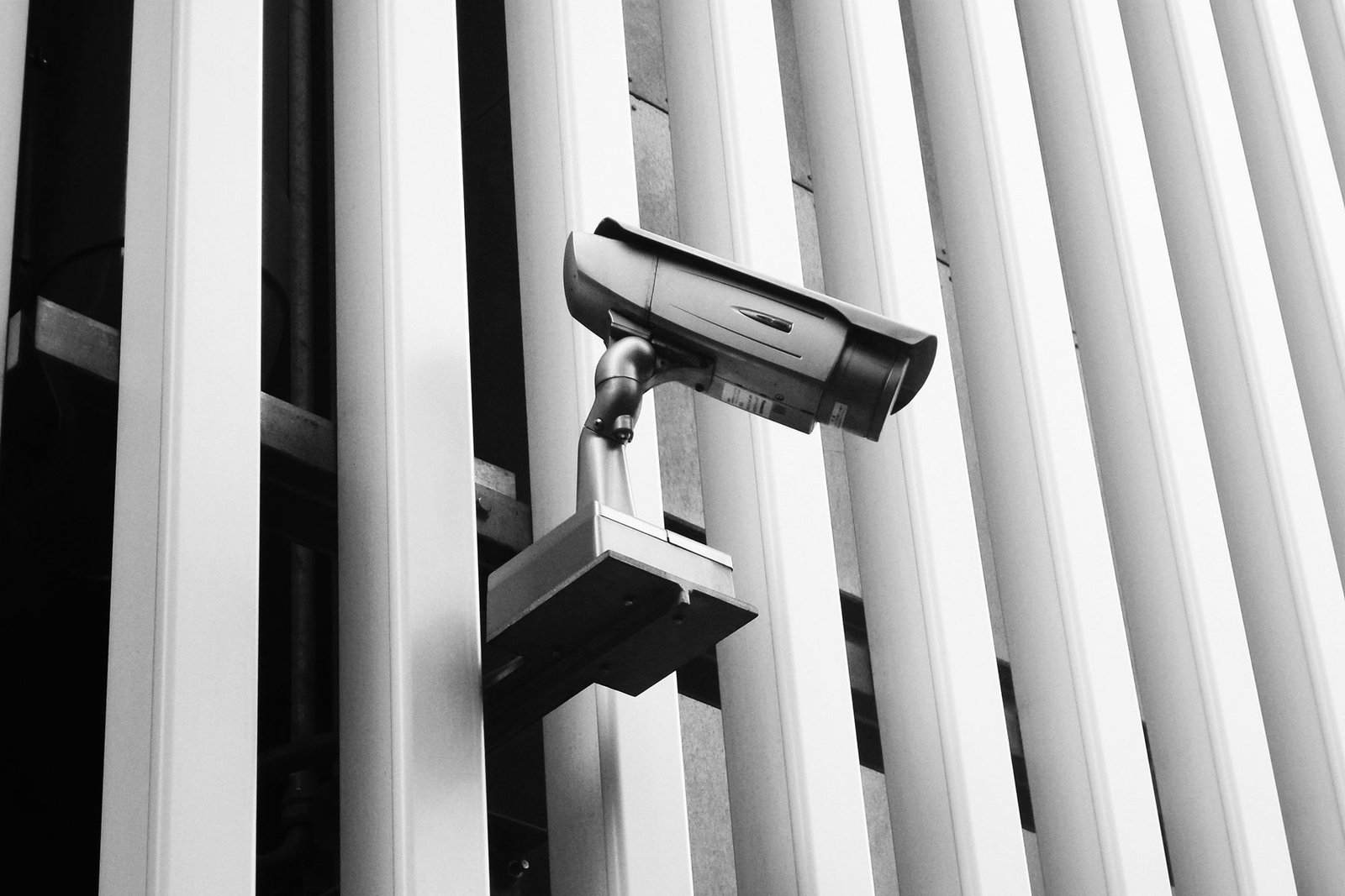 Bullet camera mounted on a stand-off bracket, held clear of a ribbed building facade